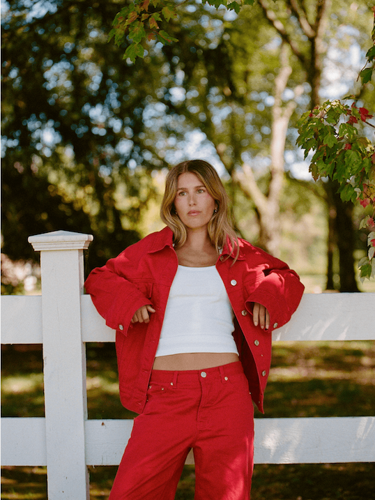 girl wearing red oversized jean jacket leaning on a fence -washed red